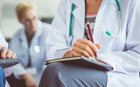 Functional Medicine Toms River NJ Doctor with Notebook HP A doctor in a white coat and stethoscope sitting cross-legged with a notebook and pen, ready to take notes.